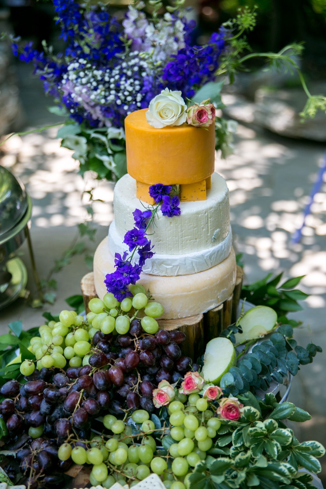 Cheese wheel celebration cake styled with grapes and fresh flowers